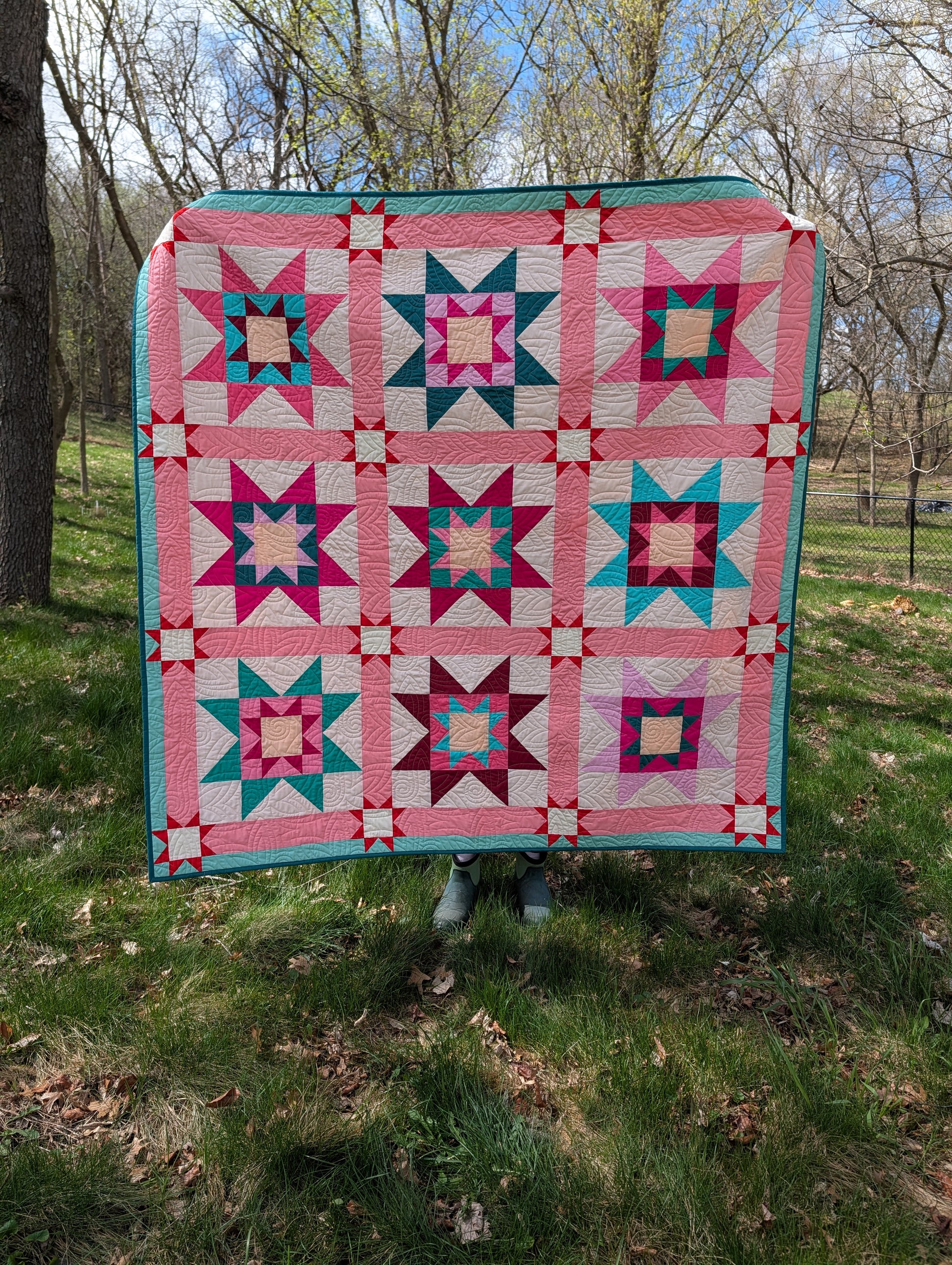 Colorful quilt with star patterns displayed outdoors on a grassy area.