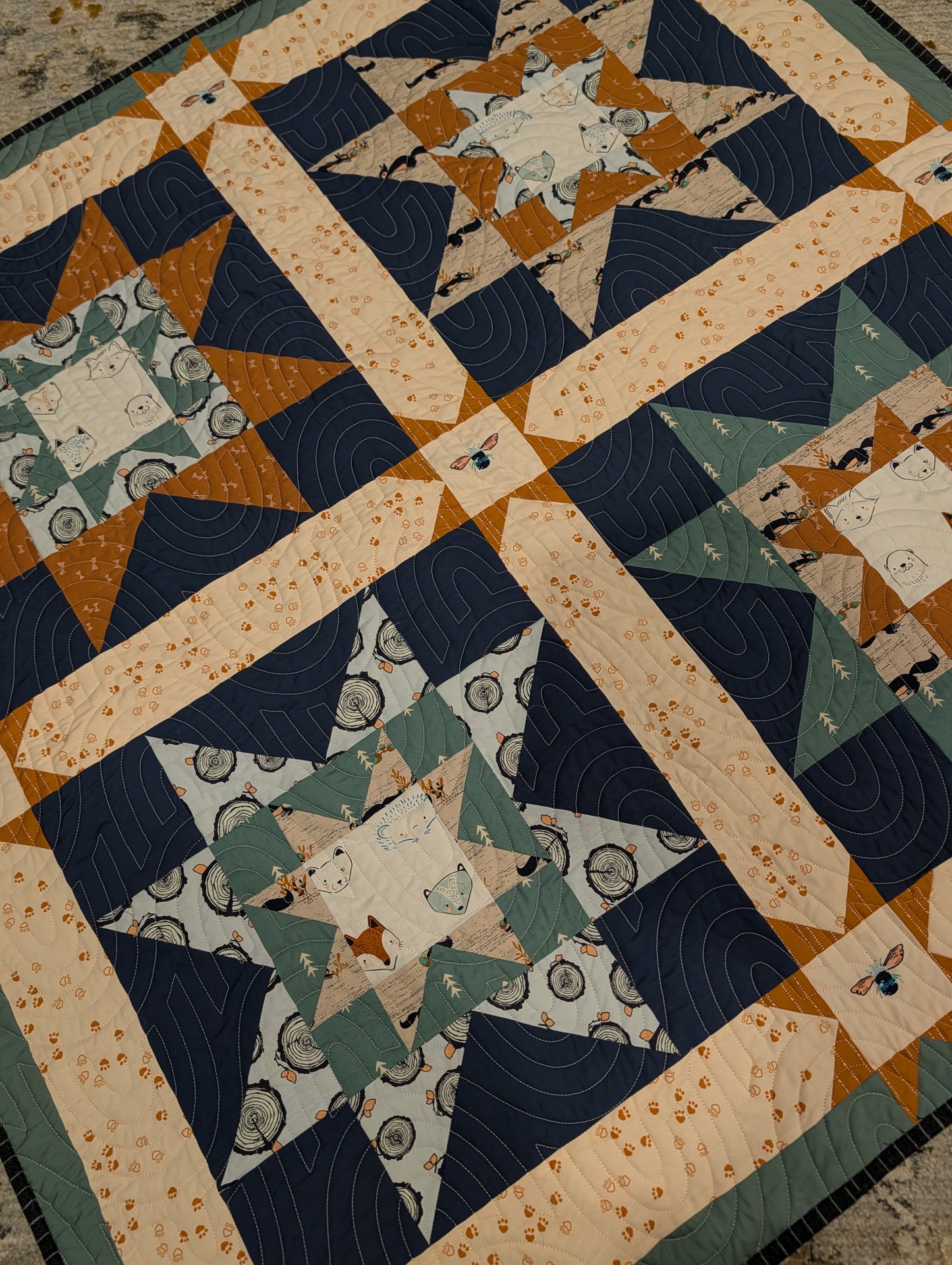 Quilt with star patterns and geometric shapes in blue, green, and brown on a beige background.