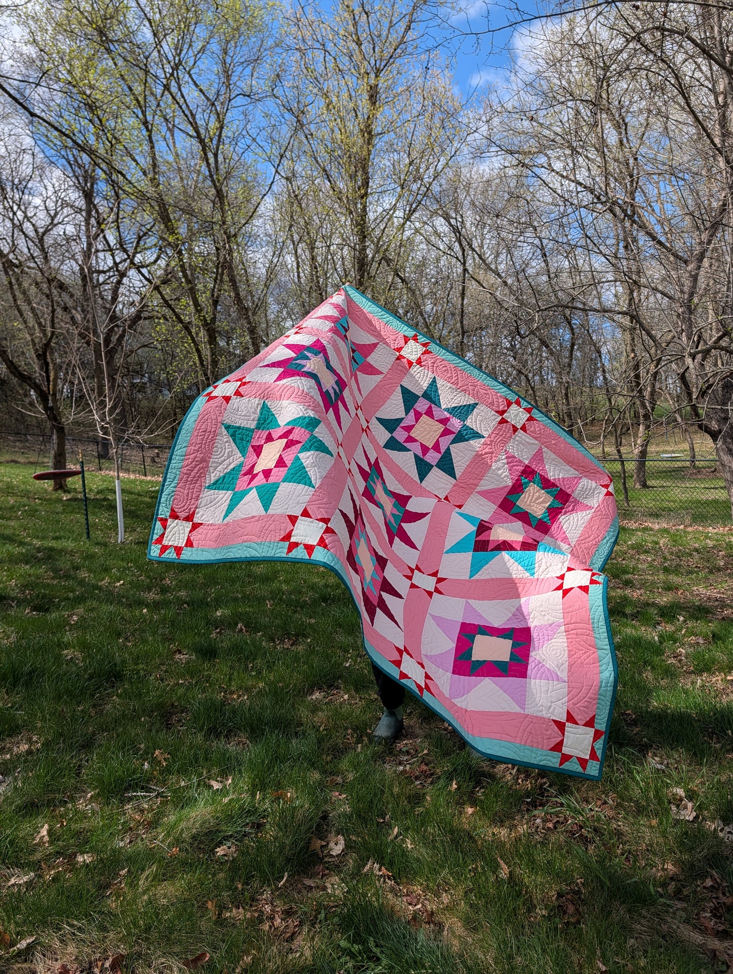 Quilt with star patterns draped over a person in a grassy outdoor setting